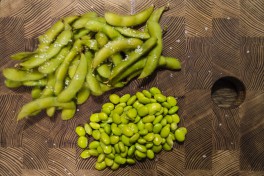 A pile of edamame in pods and a pile of already peeled kernels.